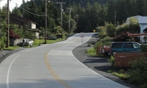 Photograph of the roadway after completion of the Shtax’Heen Roadway Improvement Project, which shows a widened roadway, fresh pavement, clearly marked lanes, and buffer areas on both sides
